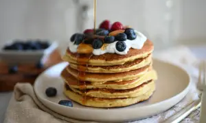 Pancake con yogurt, mirtilli, lamponi e sciroppo d'acero che cola. Un dolce inizio di giornata.