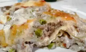 Porzione di lasagna bianca con ragù, piselli e besciamella filante, gratinata al forno.
