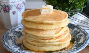 Pancake con farina di avena, una pila dorata con burro e sciroppo, serviti su un piatto decorato.
