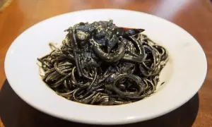 Un piatto invitante di spaghetti al nero di seppia, con anelli di calamaro e un peperoncino.