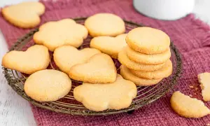 Deliziosi dolci per colazione a forma di cuore e fiore, serviti su un cestino di metallo dorato, su un tovagliolo di stoffa color prugna.