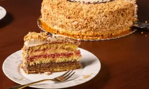 Una fetta di pizza dolce abruzzese, multistrato e ricoperta di nocciole, su un piatto bianco con una forchetta dorata.