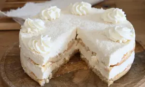 Torta soffice con strati di pan di Spagna e crema alla ricotta, ricoperta di cocco grattugiato e decorata con ciuffi di panna.