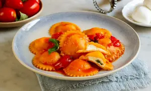 Ravioli capresi ripieni di ricotta e basilico, conditi con salsa di pomodoro fresco e guarniti con foglie di basilico.