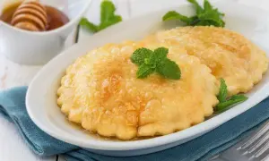 Seadas ricetta: dolci fritti dorati, guarniti con miele e menta fresca, su un piatto bianco.