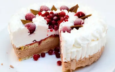 Torta gelato a strati con panna montata, frutti rossi e cioccolato. Una fetta è stata tagliata, rivelando il suo interno goloso.