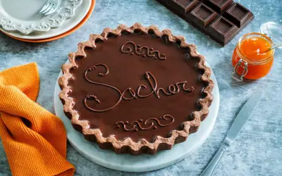 Una crostata Sacher lucida e invitante, con decorazioni in cioccolato e un vasetto di marmellata d'arancia accanto.