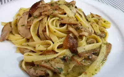 Un piatto invitante di tagliatelle ai porcini, condite con funghi freschi e prezzemolo tritato, su un piatto bianco.