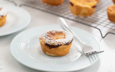 Un delizioso pastel de nata, cosparso di zucchero a velo, su un piatto azzurro con una forchetta.
