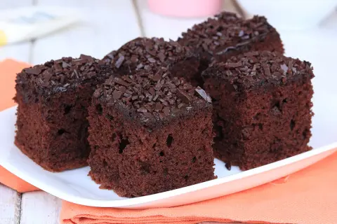 Quattro fette di torta al cioccolato morbida e umida, ricoperte di codette di cioccolato, su un piatto bianco.