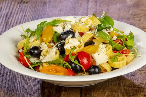 Pasta crudaiola colorata con pomodorini, olive nere, rucola e scaglie di parmigiano. Fresca e invitante.