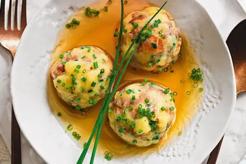 Tre canederli in brodo, guarniti con erba cipollina. Una deliziosa ricetta per un piatto tradizionale.