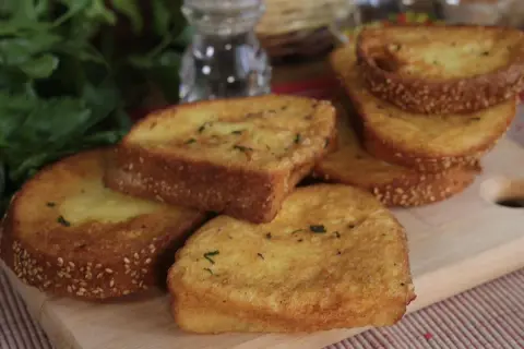 Fette dorate di pane fritto, cosparse di semi di sesamo e erbe aromatiche, pronte per essere gustate.