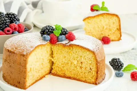 Torta soffice allo yogurt greco, decorata con frutti di bosco freschi e una spolverata di zucchero a velo.