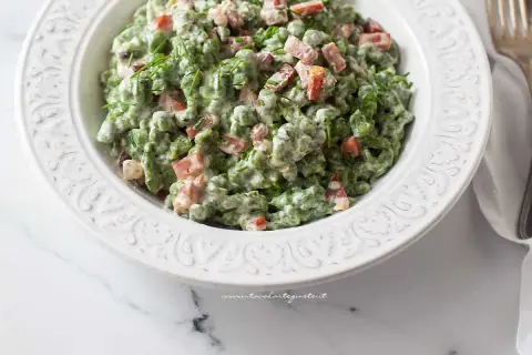 Un piatto di gnocchetti tirolesi verdi, conditi con panna, piselli e speck croccante, guarniti con erba cipollina.