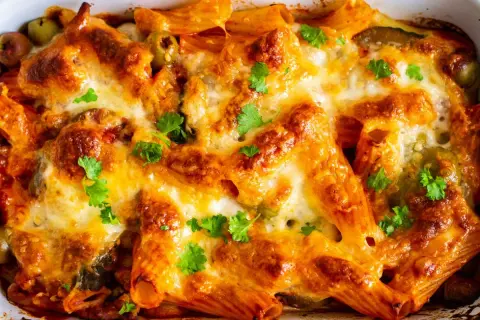Un invitante pasta al forno ricetta della nonna, dorata e filante, con olive e prezzemolo fresco.