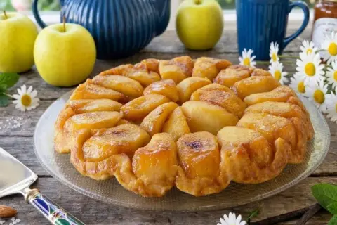 Una deliziosa tarte tatin di mele dorate, con mele fresche, una teiera blu e fiori di campo.