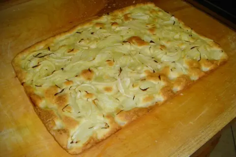 Focaccia con cipolle appena sfornata, dorata e fragrante, adagiata su un tagliere di legno.