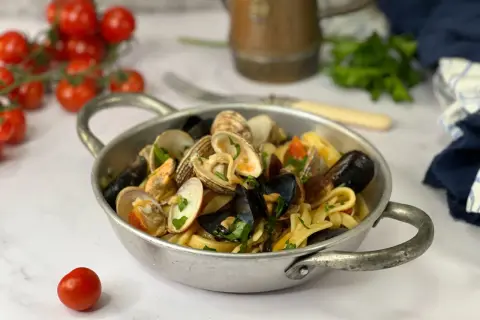 Un piatto di scialatielli ai frutti di mare, con cozze, vongole e pomodorini, guarnito con prezzemolo fresco.