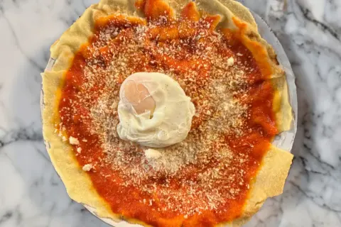 Piatto con pane carasau, salsa di pomodoro, formaggio grattugiato e uovo in camicia. Un'idea per gustose ricette.