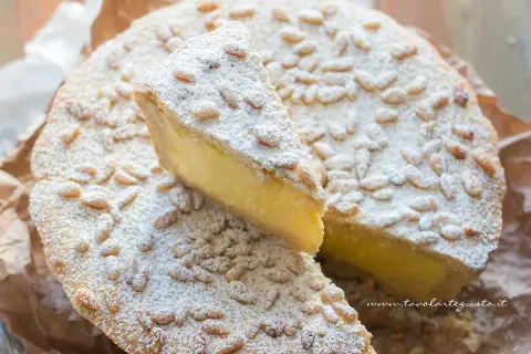 Una fetta di torta della nonna, cosparsa di pinoli e zucchero a velo, mostra il suo ripieno cremoso.