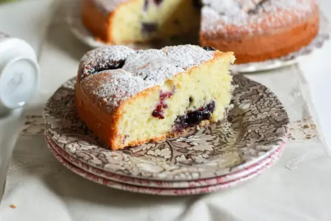 Una fetta di torta nua soffice, cosparsa di zucchero a velo, con un cuore di marmellata di frutti di bosco.