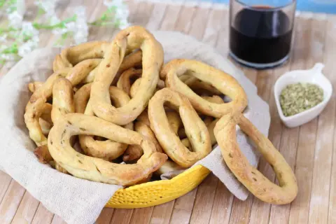 Taralli al finocchietto con lievito, croccanti e profumati, in un cestino con un bicchiere di vino rosso e semi di finocchio.