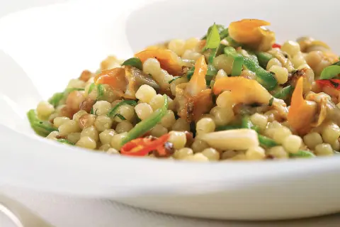 Un piatto di fregola sarda con vongole, peperoncino e zucchine, un sapore di mare e terra.