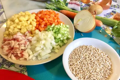 Ingredienti pronti per una saporita minestra d'orzo: orzo perlato, patate, carote, sedano, cipolla e pancetta.