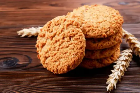 Biscotti integrali dorati e croccanti, impilati su un tavolo di legno scuro, con spighe di grano a decorare.