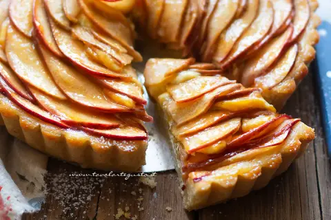 Una deliziosa crostata di mele, con fette di mela lucide disposte a spirale su una base dorata. Una fetta è stata tolta, rivelando la morbidezza.