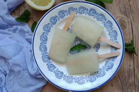 Tre ghiaccioli al limone fatti in casa su un piatto decorato, con limone e menta fresca. Perfetti per un'estate rinfrescante.