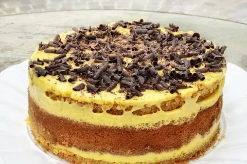 Torta pazientina a strati, con crema gialla e riccioli di cioccolato fondente in cima.