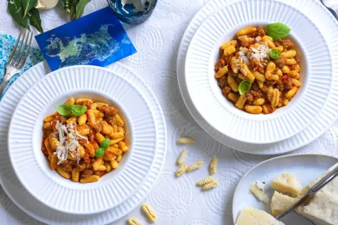 Due piatti di malloreddus alla campidanese, pasta sarda con sugo di salsiccia e pomodoro, guarniti con basilico e parmigiano.