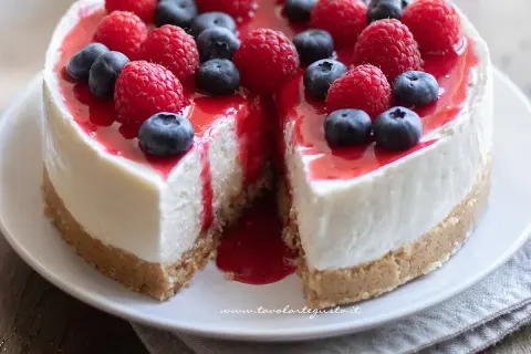 Delizioso cheesecake con mascarpone, guarnito con lamponi freschi, mirtilli e una colata di salsa rossa.