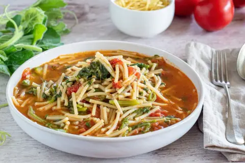 Piatto di pasta con i tenerumi asciutta, pomodoro e verdure fresche, pronto per essere gustato.