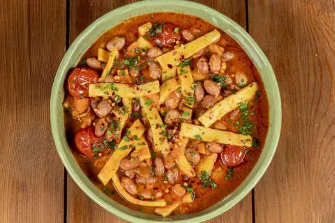 Piatto di sagne e fagioli fumante, con pomodorini e prezzemolo tritato, servito in una ciotola verde su un tavolo di legno.