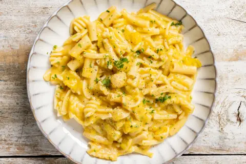 Piatto di pasta e zucca cremosa, guarnita con prezzemolo tritato e pepe nero, servita su un piatto bianco con bordo decorato.