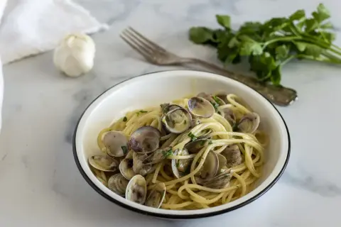 Un piatto invitante di spaghetti con le vongole, conditi con prezzemolo fresco e serviti in una ciotola bianca.