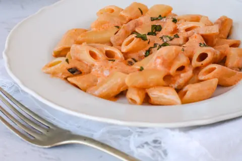 Piatto di penne alla vodka cremose, guarnite con erbe fresche, pronte per essere gustate con una forchetta.