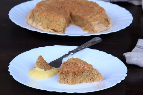Una fetta di torta nocciole piemontese originale, soffice e dorata, servita con crema gialla.