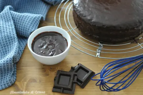 Torta ricoperta di lucida ganache cioccolato per copertura, con ciotolina di ganache, cioccolato fondente e frusta blu.