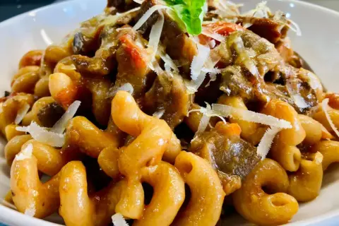 Un piatto invitante di pasta con melanzane, condita con un ricco sugo e scaglie di parmigiano.