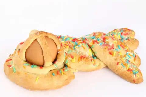 Una cuzzupa intrecciata con un uovo al centro, decorata con zuccherini colorati.