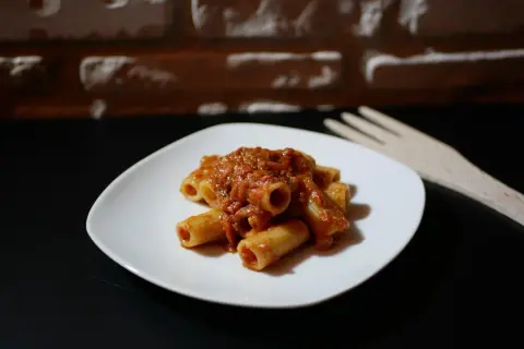 Piatto di pasta alla portofino con sugo rosso e forchetta in legno sullo sfondo di mattoni.