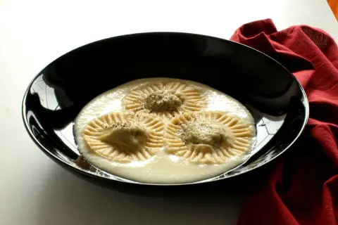 Tre ravioli di borragine, con un ripieno cremoso e una spolverata di pepe, serviti in una ciotola nera su un tovagliolo rosso.