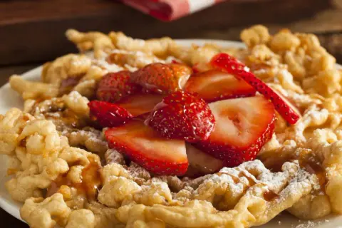 Strauben croccanti, guarniti con fragole fresche e zucchero a velo. Una deliziosa ricetta per un dolce da fiera.