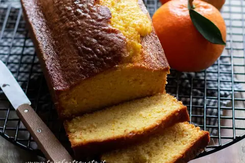 Plumcake all'arancia appena sfornato, dorato e profumato, con fette morbide e arance fresche accanto.