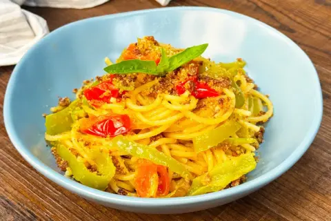 Spaghetti con friggitelli, pomodorini e mollica tostata, guarniti con basilico fresco. Un piatto semplice e gustoso.