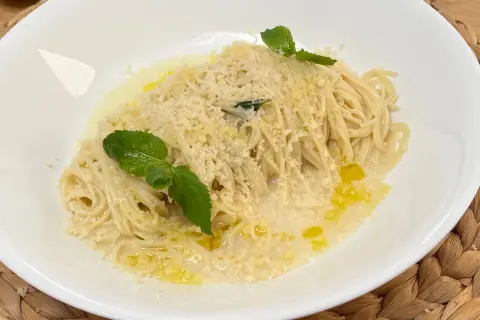 Spaghetti al limone, conditi con parmigiano grattugiato, olio d'oliva e guarniti con foglie di menta fresca.